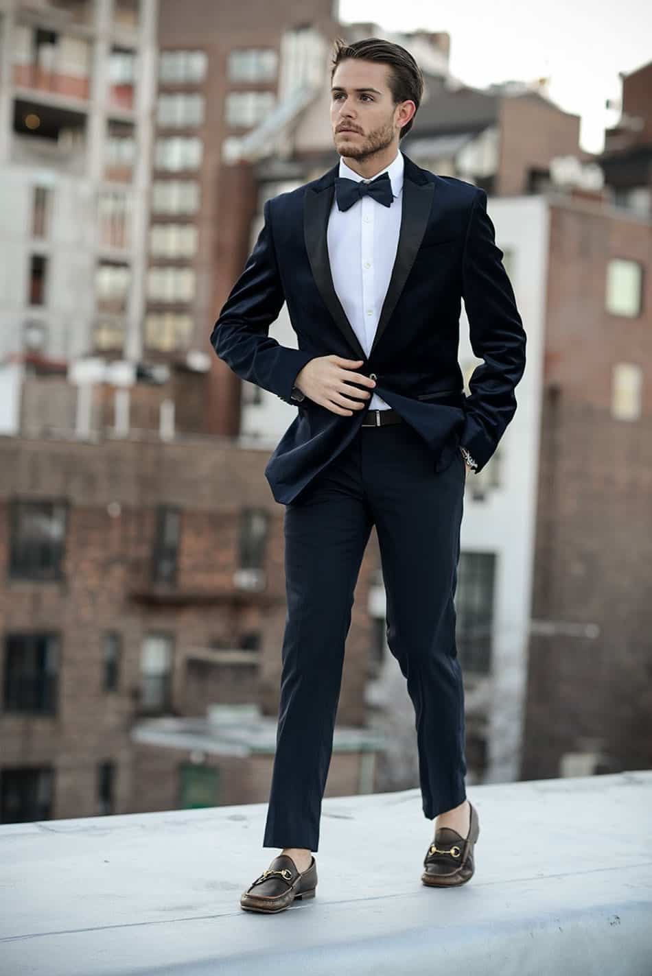 A man confidently posing in a navy tuxedo with bow tie