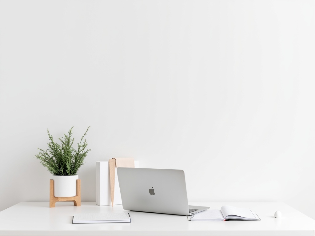 A modern, minimalist home office desk featuring a laptop, notepad, and small potted plant against a white background.