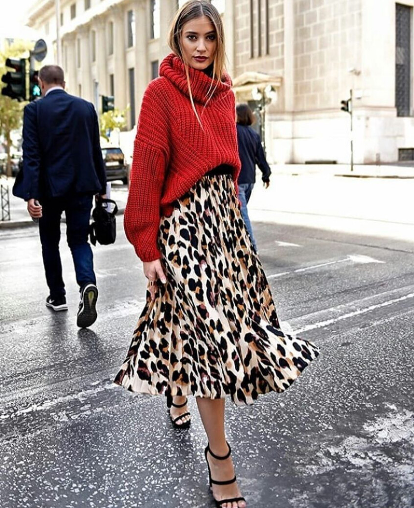 A woman wearing a red sweater and leopard print skirt on the street.